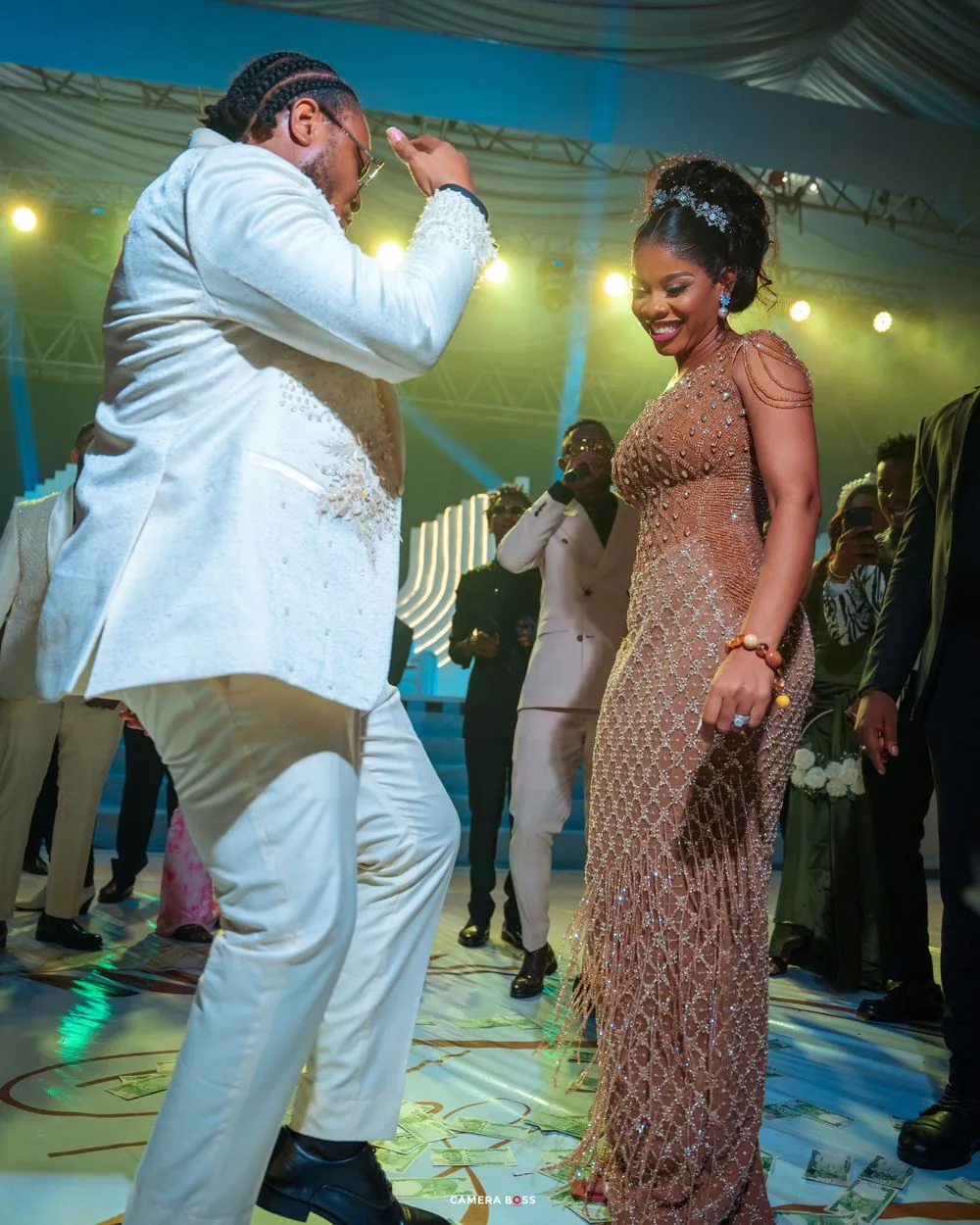 Well-dressed dancers moving enthusiastically on an illuminated dance floor under a draped tent ceiling with string lights.