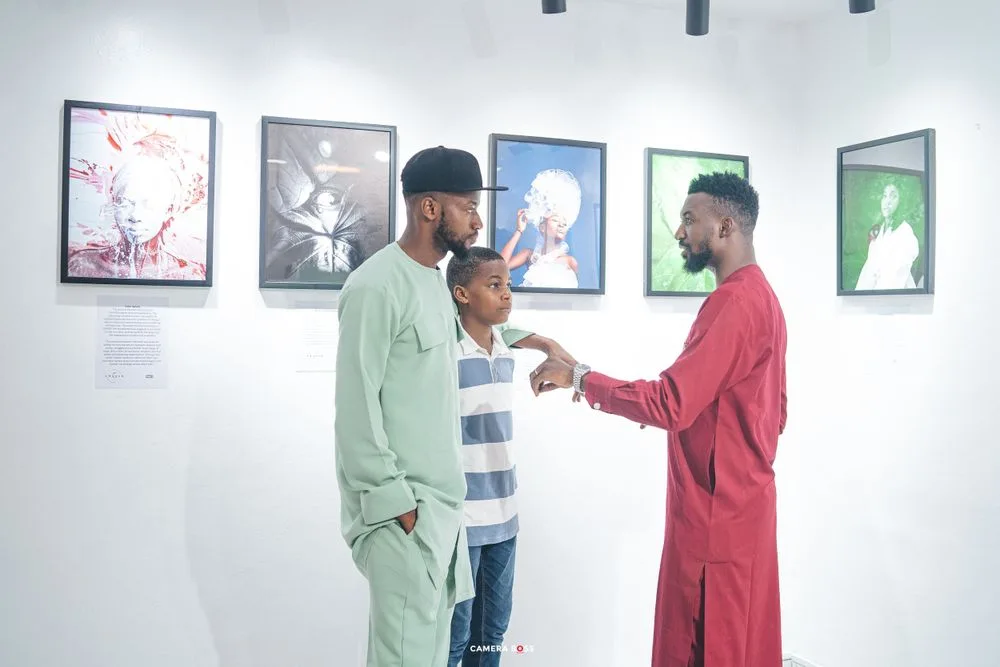 People having an animated conversation in front of colorful framed artwork displayed in a gallery.