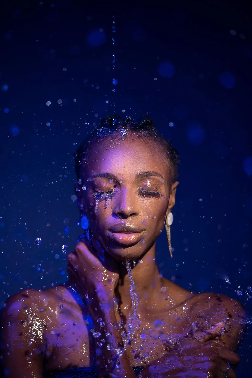 Artistic beauty portrait with blue and purple lighting effects showing glitter and water droplets against dark background.