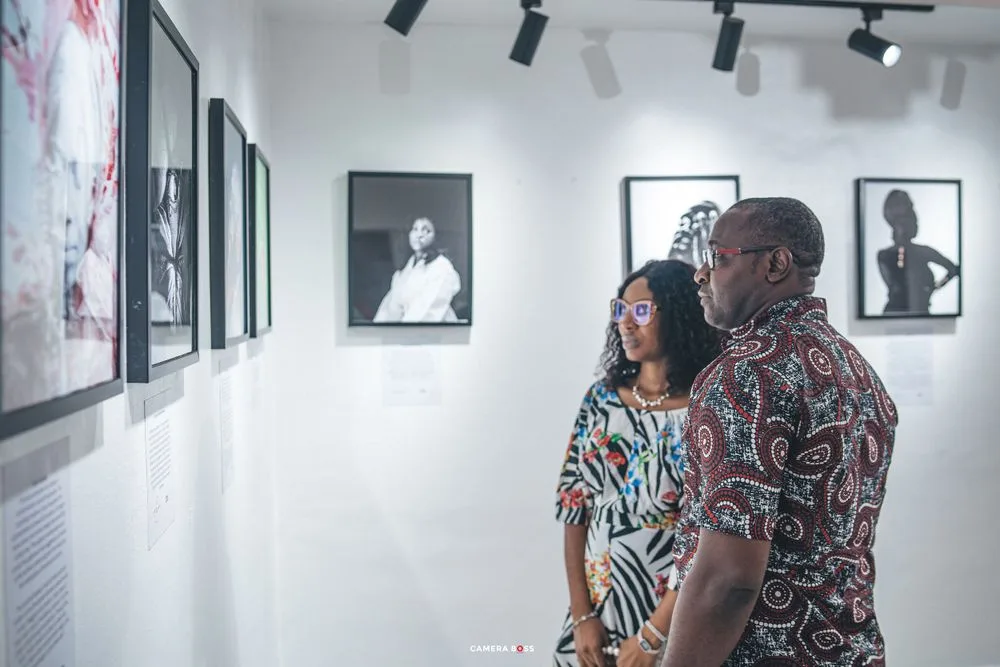 Two people view black and white portrait photographs displayed in a modern white-walled art gallery.