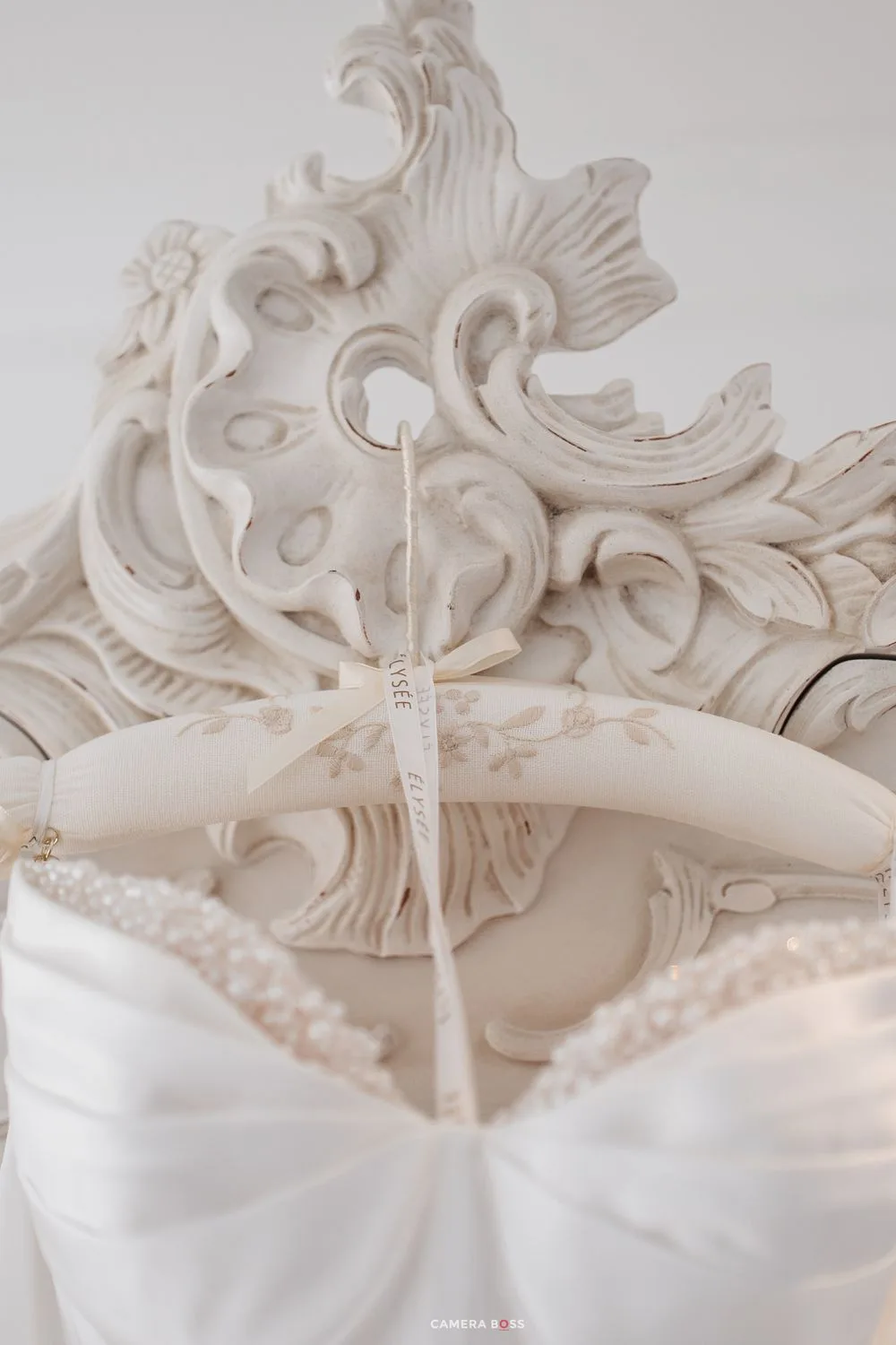 Ornate white baroque mirror with decorative wedding dress hanger and beaded bridal gown detail.