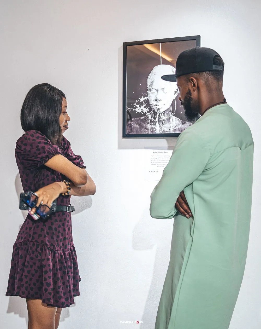 People having a friendly conversation while standing in an art gallery with framed artwork on display.