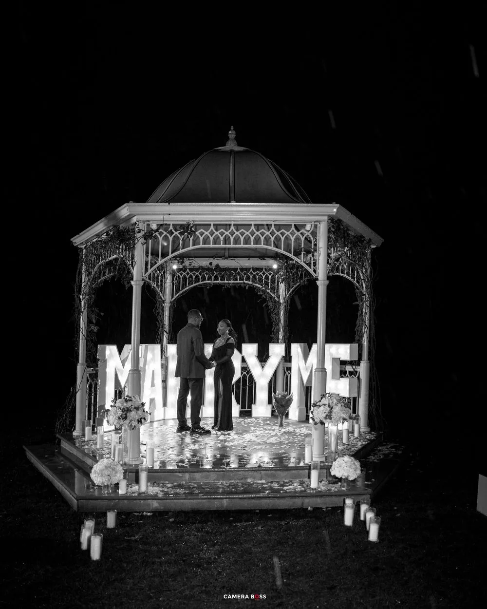 A vintage black and white photo of a decorated gazebo with illuminated 'MAILTIME' text display and candles at night.