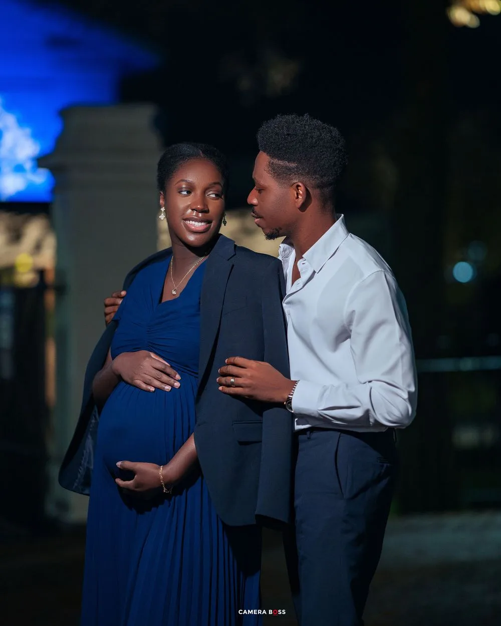 Couple in formal attire share an intimate nighttime moment outdoors as they expect their first child.