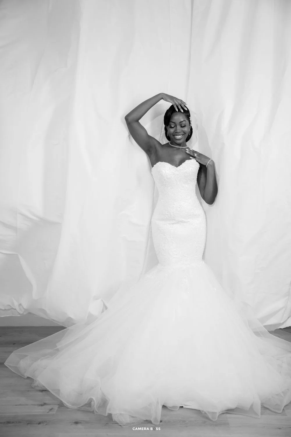 A stunning bride poses in a white strapless mermaid wedding gown with tulle skirt against a light backdrop.