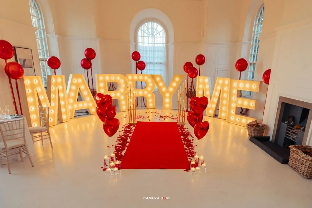 Wedding ceremony setup with illuminated LOVE letters, red balloon decor and red carpet aisle in an elegant white room.
