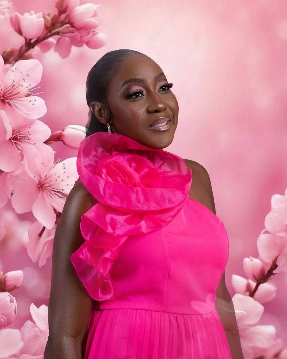A person in a vibrant hot pink one-shoulder dress poses against a soft pink background with cherry blossoms.