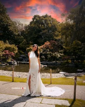 A white wedding dress glows against a dramatic sunset in a serene Japanese garden with a tranquil pond.