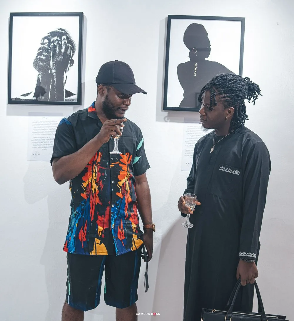Two people having a conversation while standing in front of black and white framed artwork displayed on a white wall.