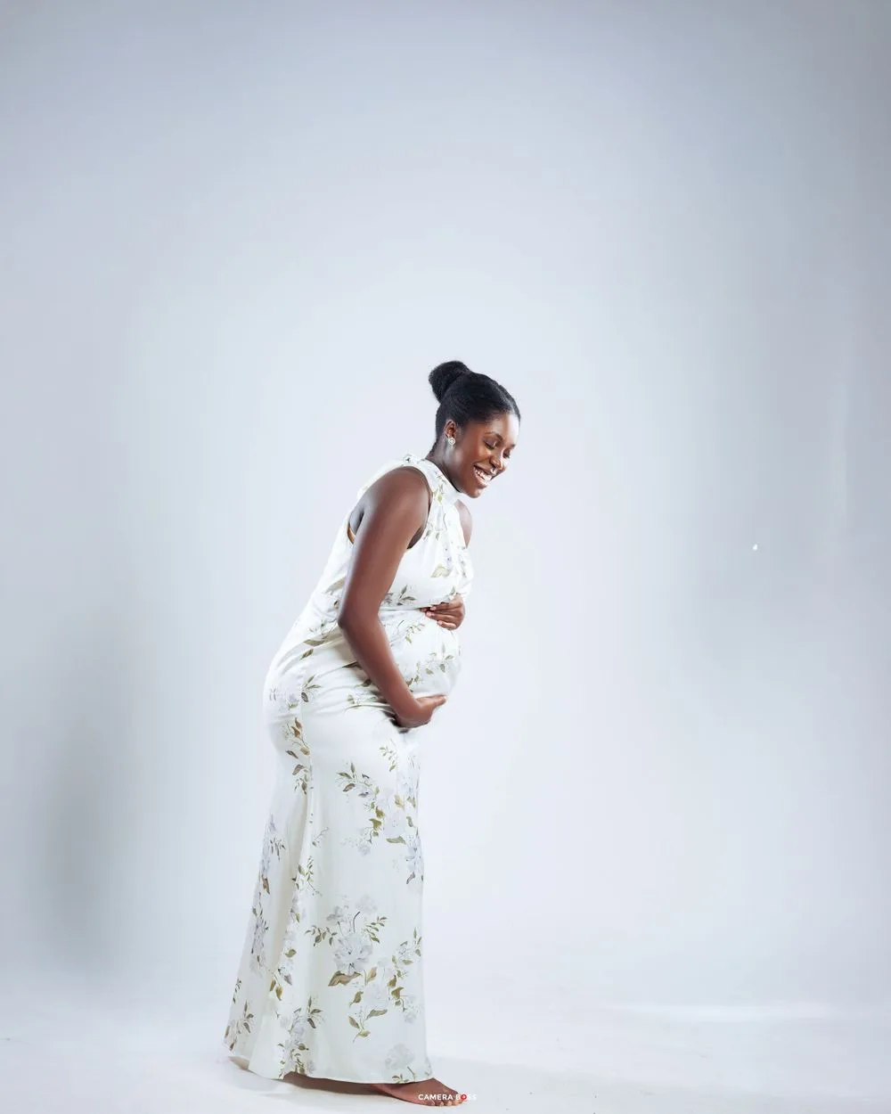 A person in a white floral dress with sleeves poses in a side profile against a light gray background.