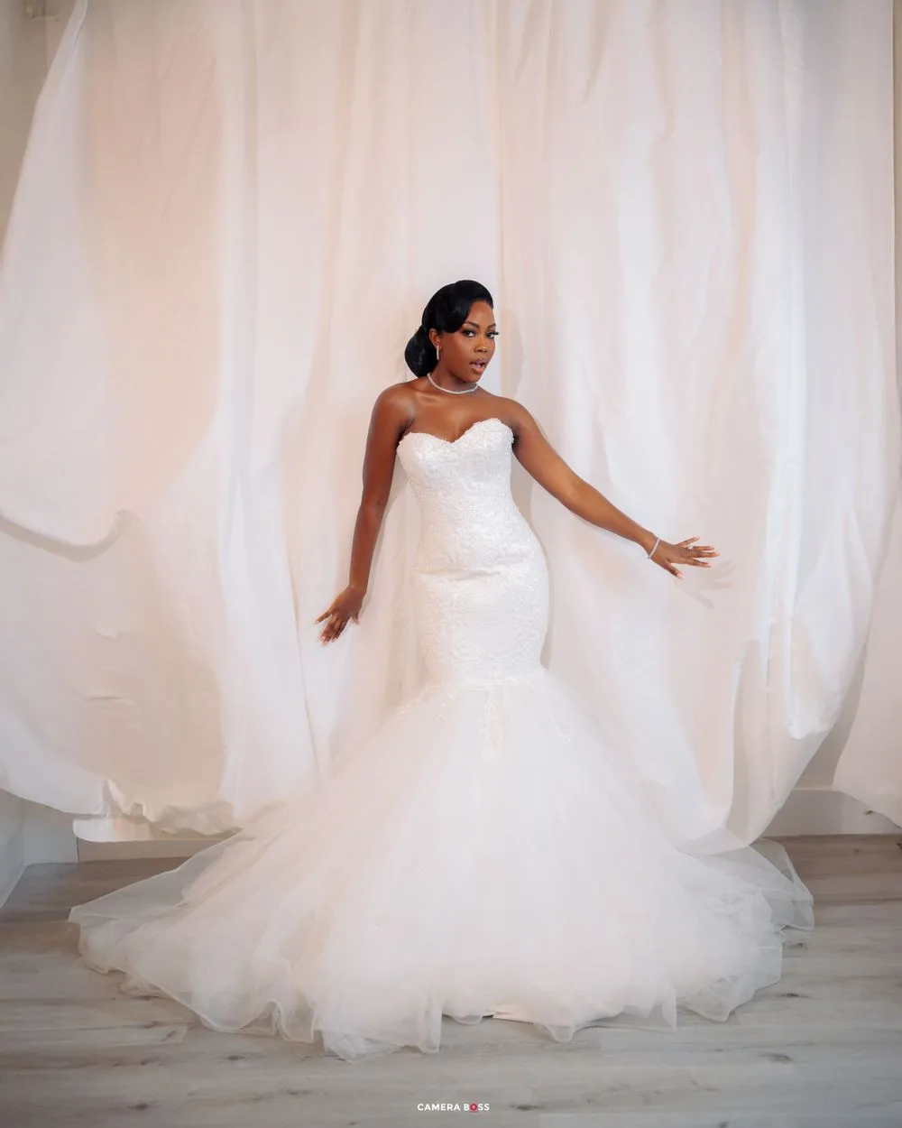 A stunning mermaid-style wedding dress with a strapless sweetheart neckline and flowing tulle skirt on display against white drapes.