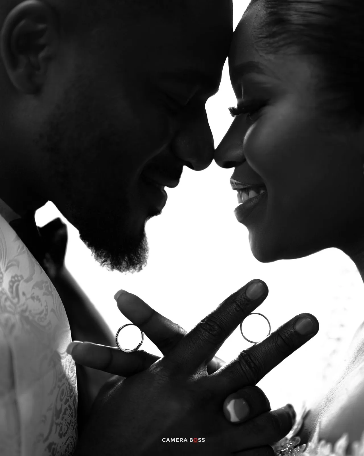 Black and white profile portrait of a romantic couple in white outfits smiling and touching foreheads together.