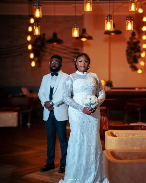 Elegant newlyweds pose together in a warmly lit venue with hanging lanterns and a romantic ambient atmosphere.