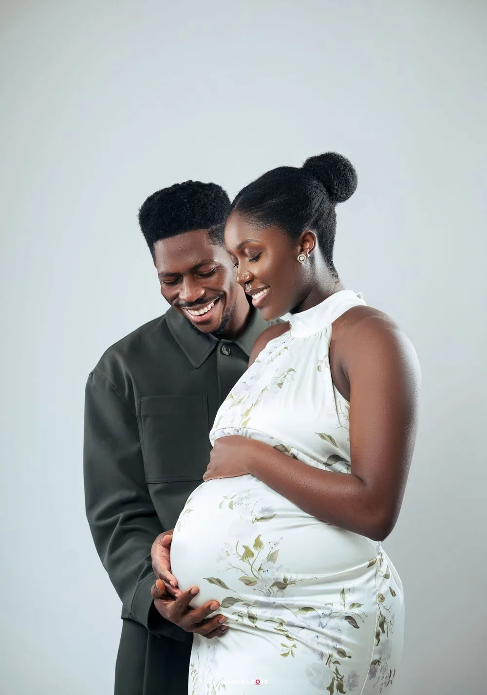 Expectant couple stands together lovingly against white backdrop as they embrace the pregnant belly in a tender moment.