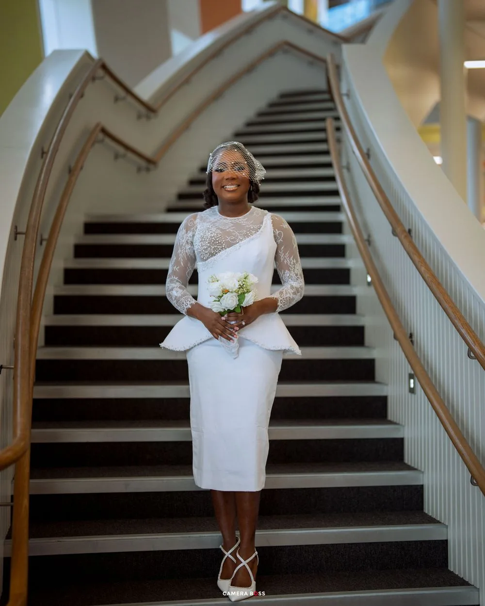 A white short wedding dress is displayed on a grand staircase with black and white striped steps.