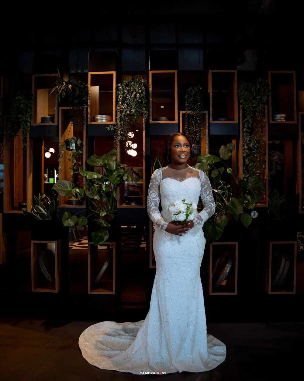 A series of elegant wedding photos displayed in wooden frames on a dark wall with ambient lighting and greenery.