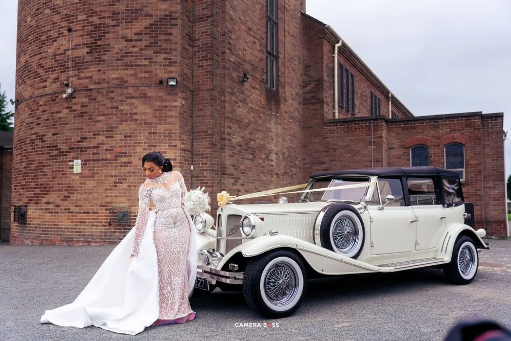 A classic vintage white Rolls Royce wedding car parked in front of a brick church building.