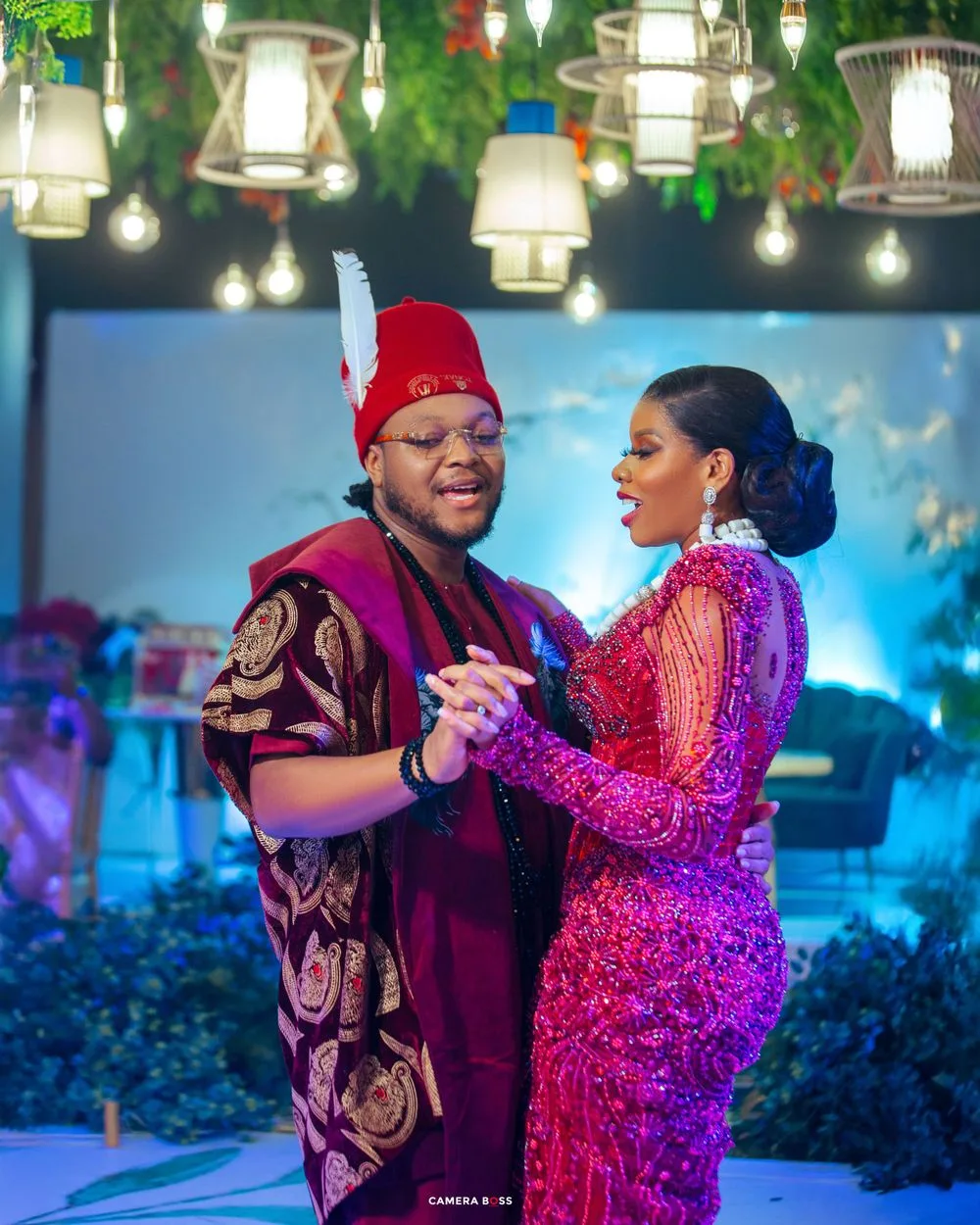 A couple dances together at an evening event with decorative lanterns and lights hanging above.