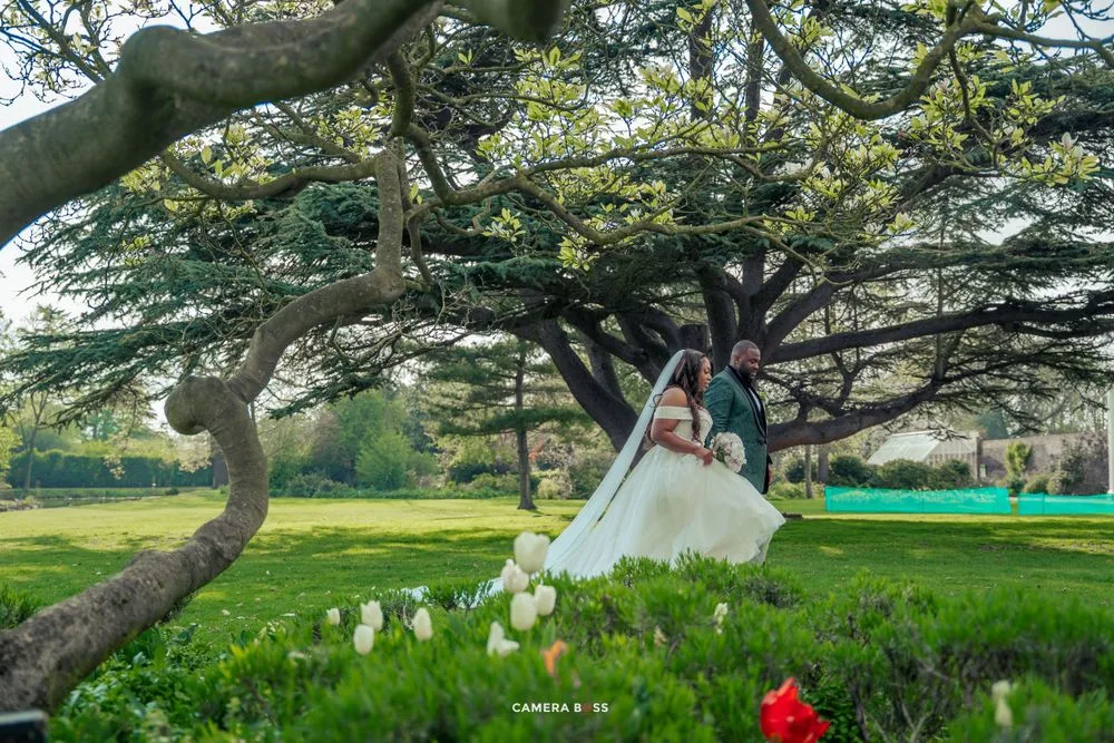 Couple enjoying a tranquil moment under a sprawling tree with a white floral setup in a lush garden setting.