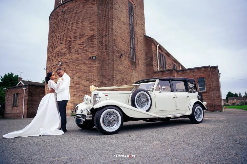 An elegant vintage cream-colored wedding car parked outside a brick church building.