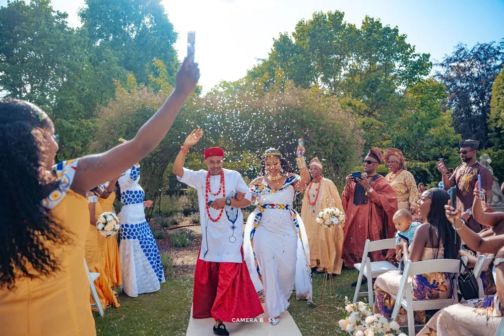 Wedding guests celebrate with dancing and raised hands during an outdoor garden ceremony in natural sunlight.
