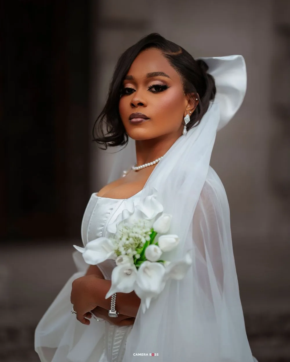 Bride in white wedding gown with flowing veil poses elegantly for bridal portraits.