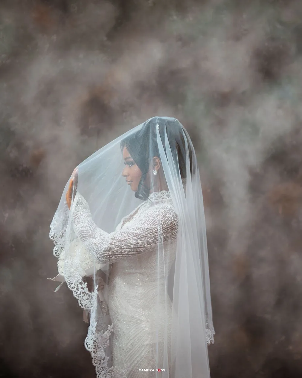 Close-up details of delicate bridal veil with lace trim against a moody gray background.
