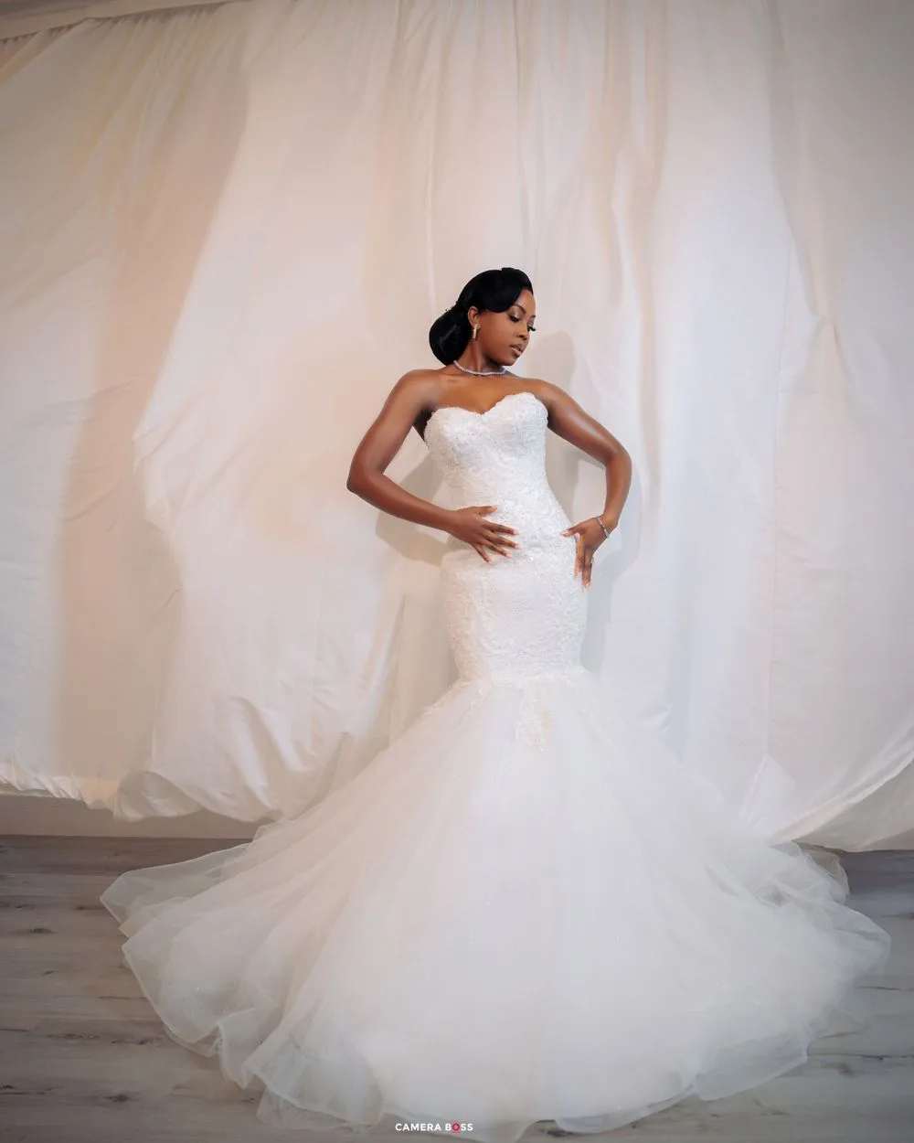 A stunning white mermaid wedding gown with sweetheart neckline and flowing tulle train against a light backdrop.