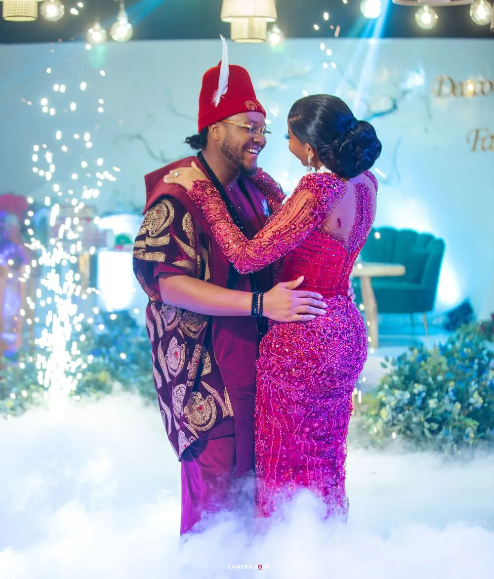 A couple in red formal attire dancing together on stage with sparkling effects and lighting in a festive setting.