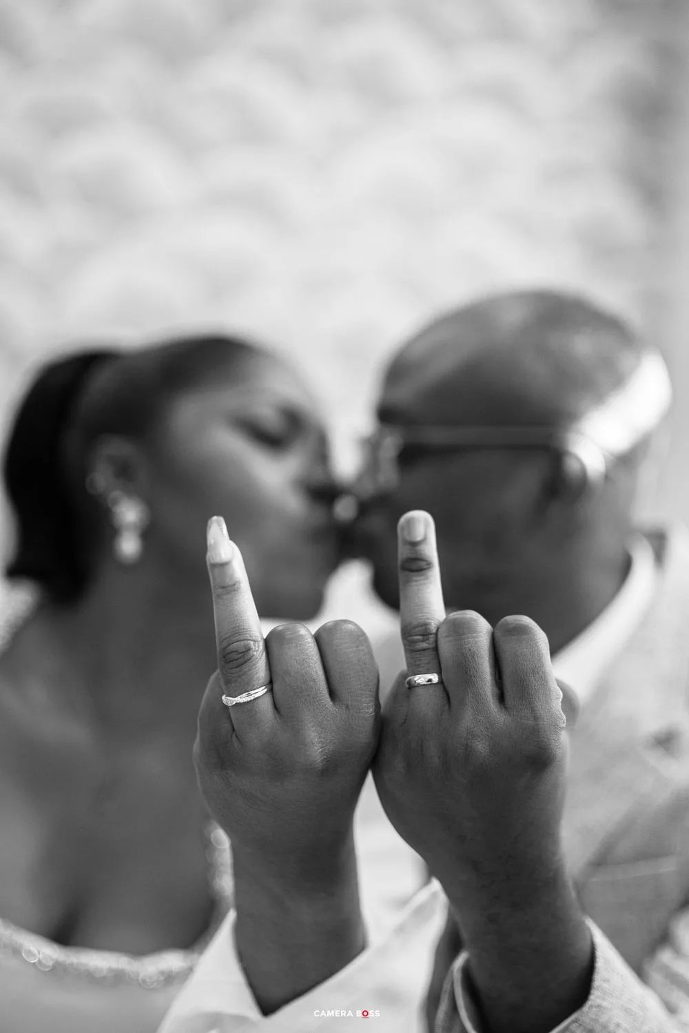 A close-up black and white photo of two hands showing wedding rings while making middle finger gestures together.