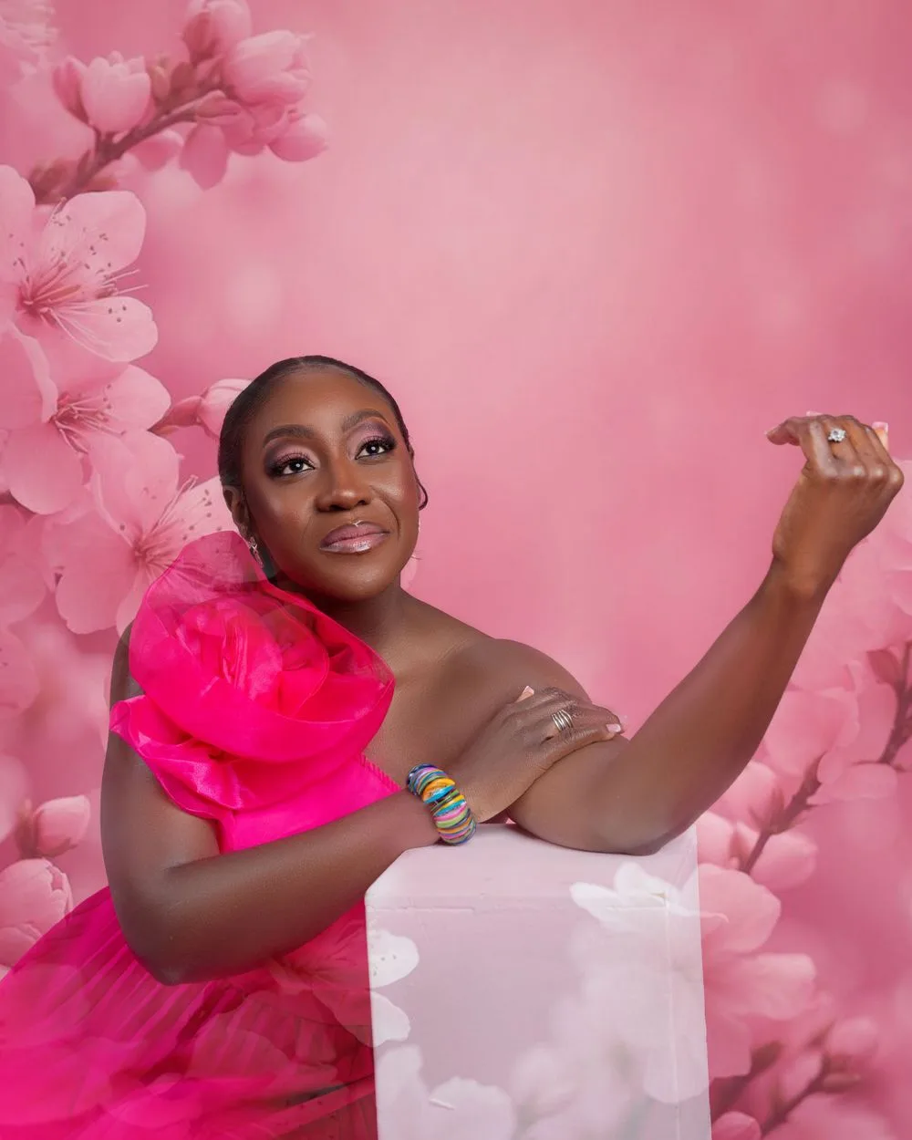 A joyful posed portrait against a pink floral backdrop with cherry blossoms and wearing a vibrant pink tulle dress.