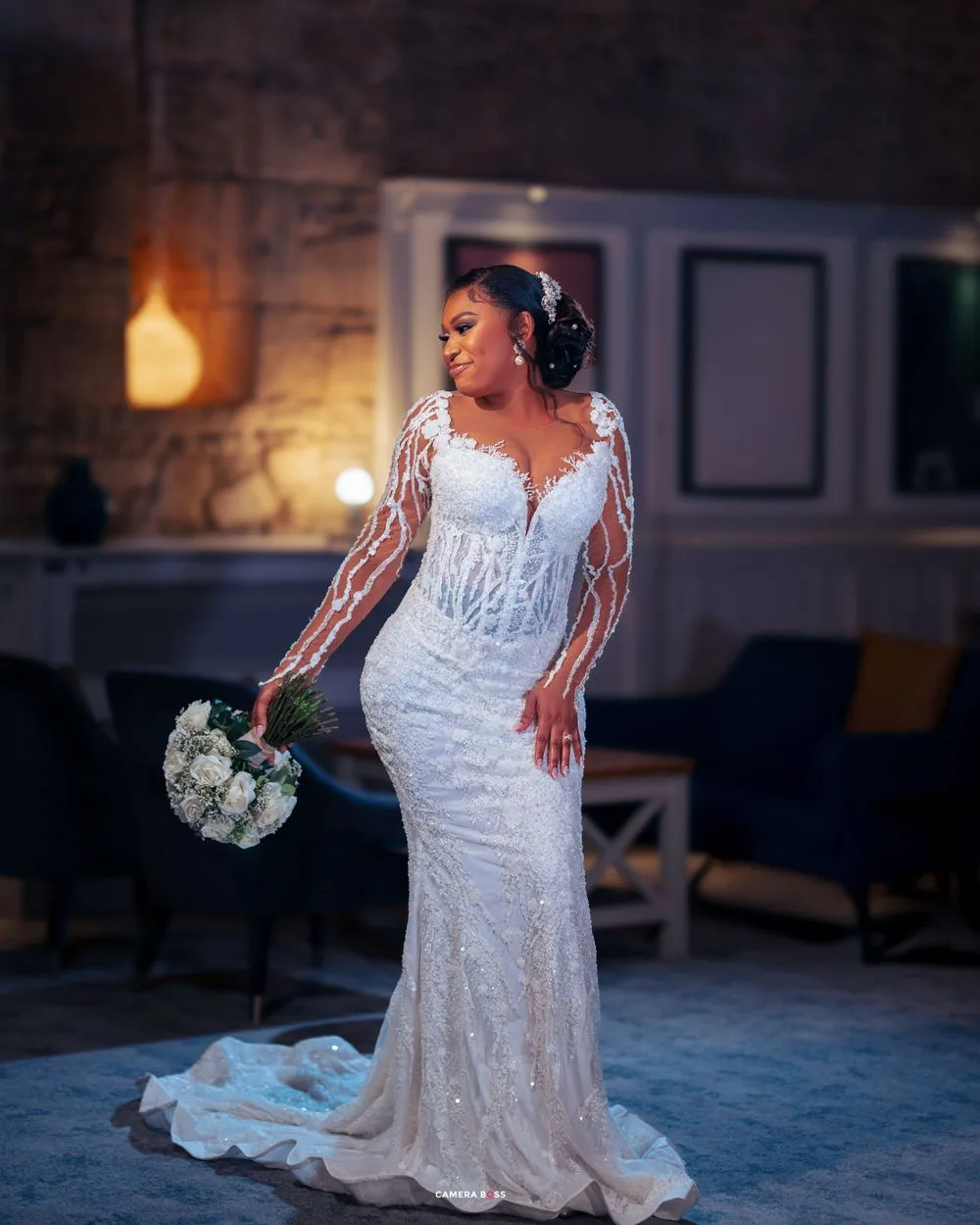 A bride poses in a stunning white lace mermaid wedding gown with long sleeves while holding a white bouquet.