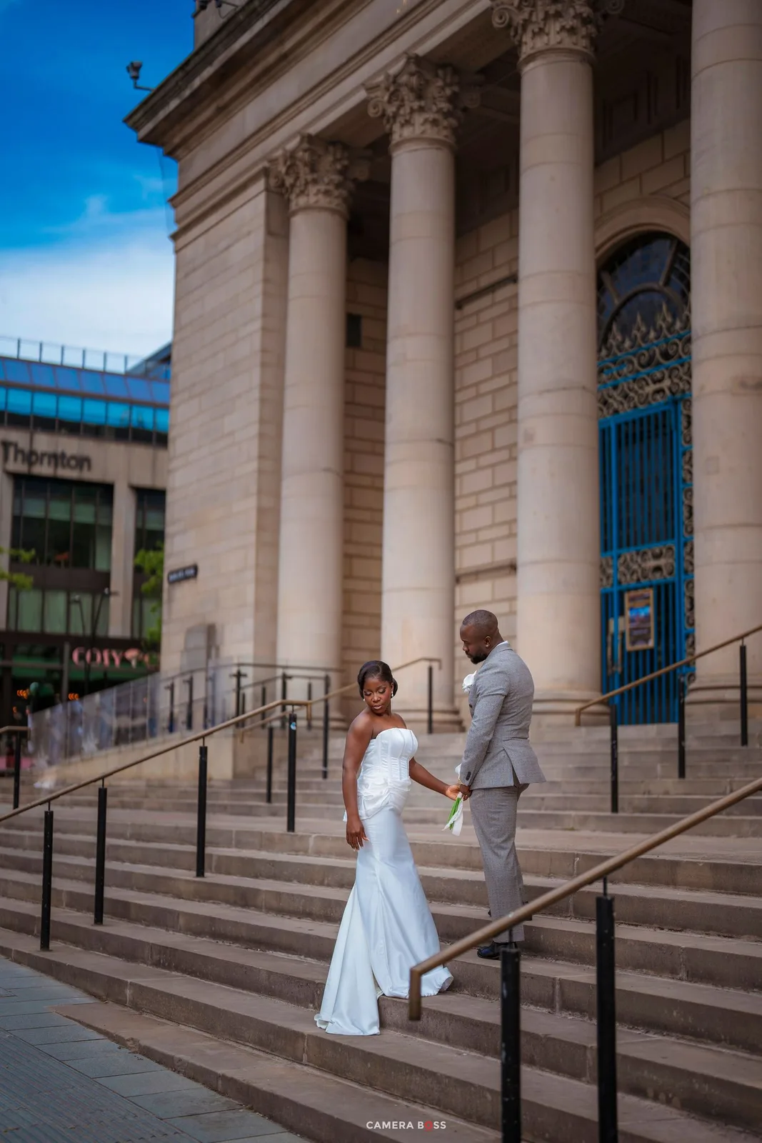 Newlywed couple in wedding attire posing on steps of grand neoclassical building.