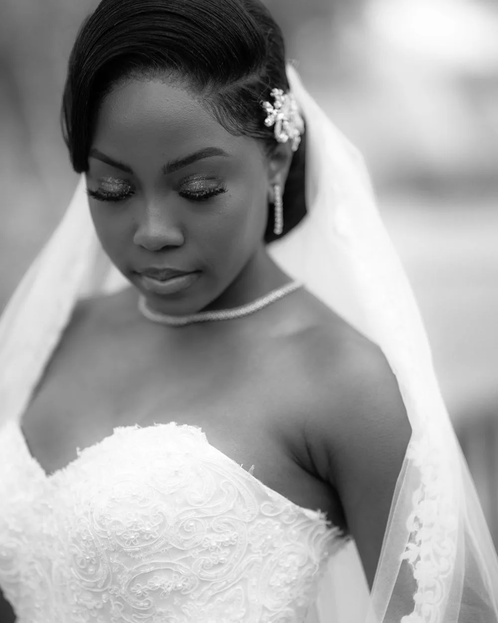 Black and white portrait of a bride in a strapless lace wedding gown with veil and floral hair accessory on her special day.